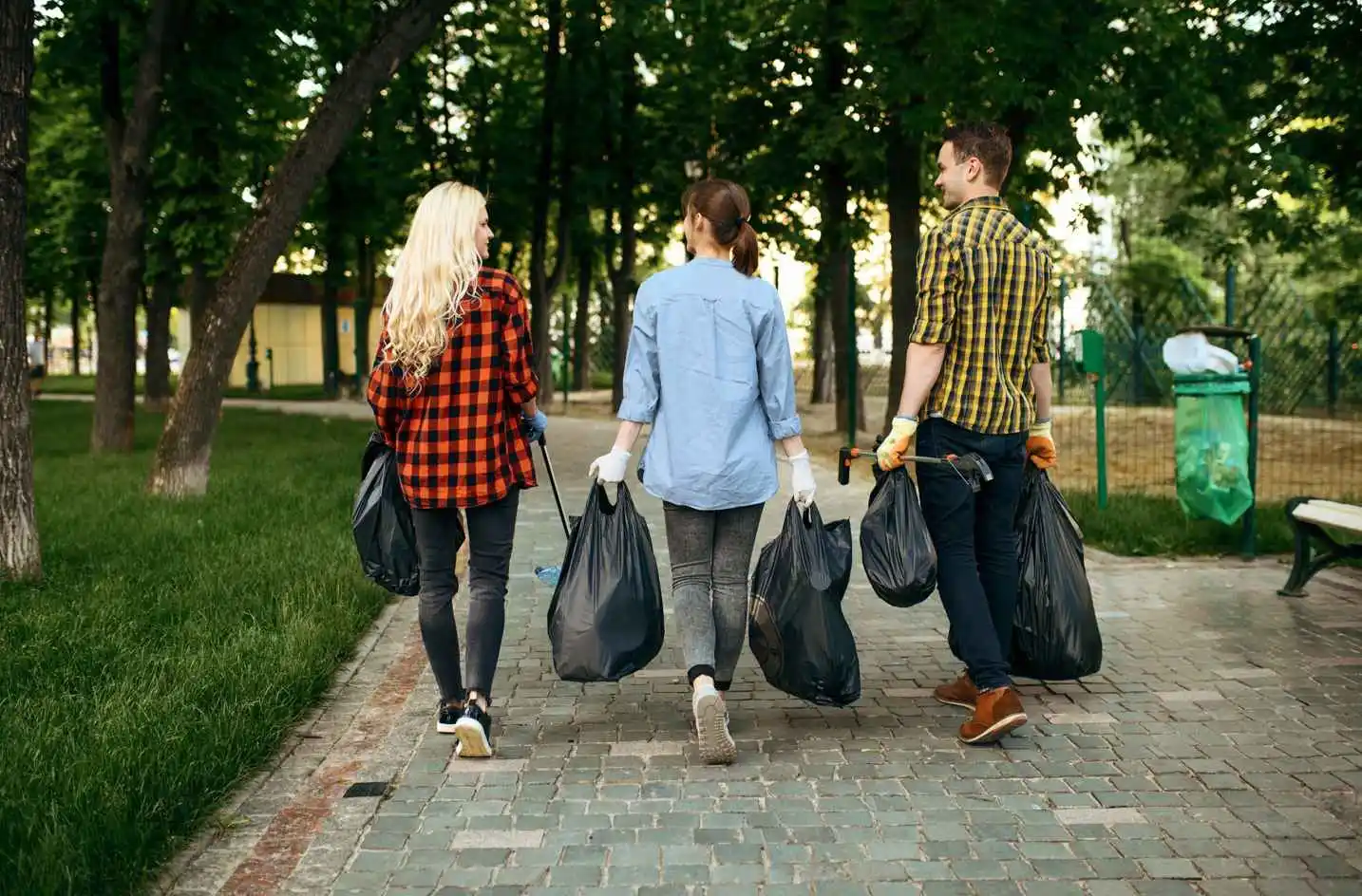 Young motivated volunteers with plastic trash bags in park