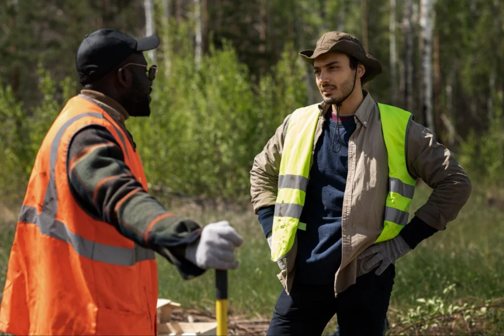 Two volunteers in reflective vests having a discussion during a forest restoration activity, surrounded by trees and natural greenery.