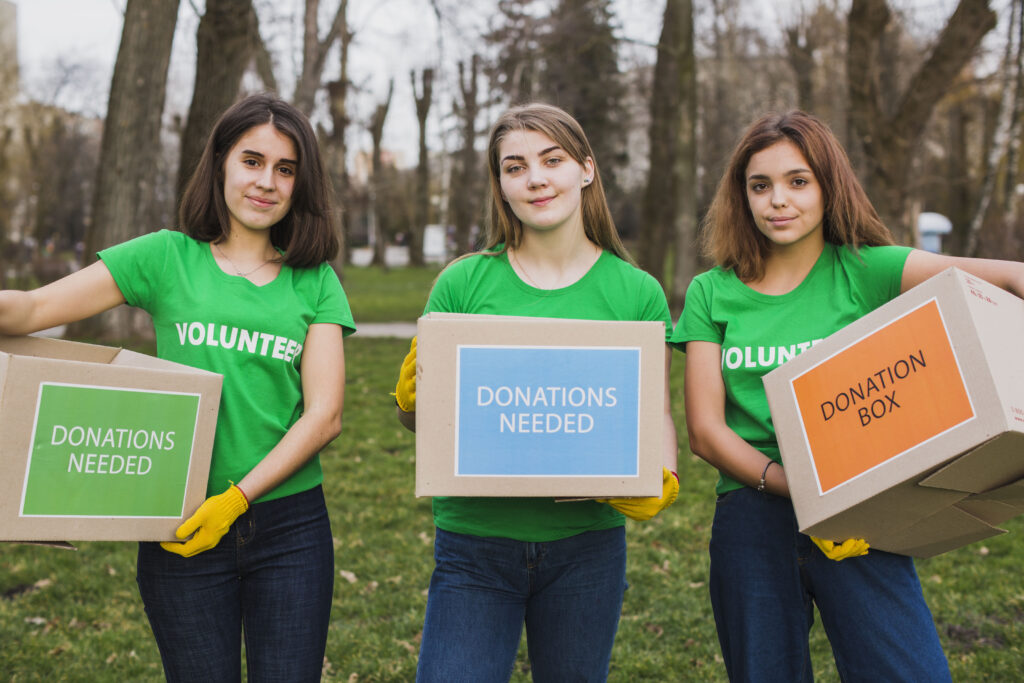 Three female teenage volunteers holding donation boxes.