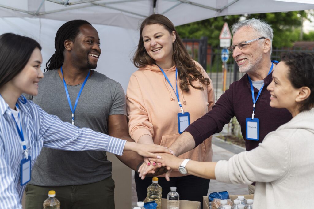 a group of volunteers smiling and stacking their hands on top of each other in the spirit of teamwork