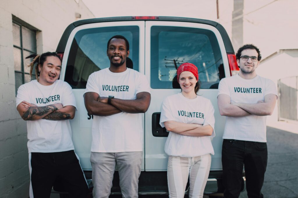 Volunteers smiling with their arms crossed in accomplishment in front of a van.