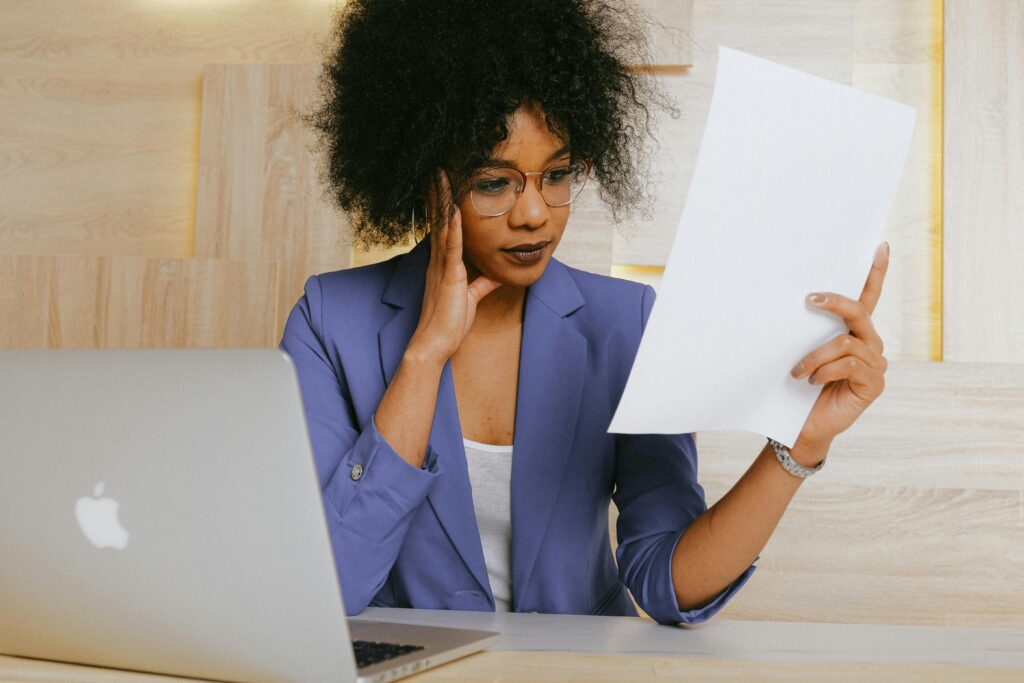 a hiring person looking at a paper resume while sitting in front of her laptop
