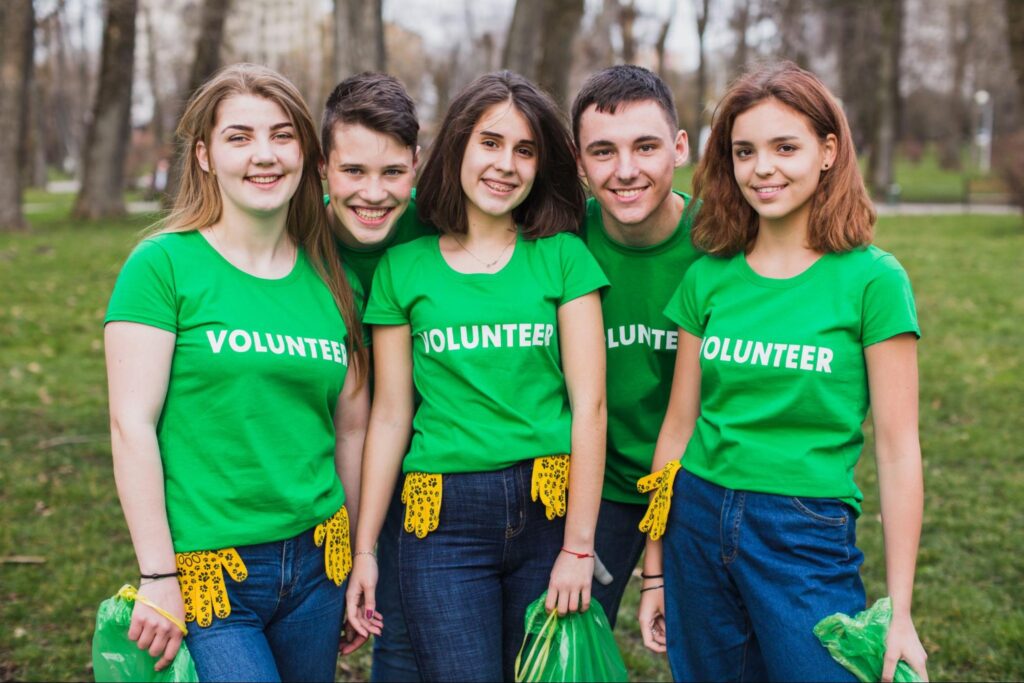 Group of young volunteers in matching green shirts posing after a park cleanup, showing teamwork and community spirit