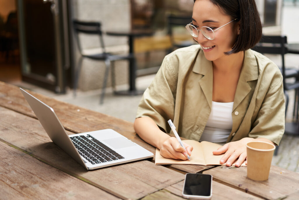 A person looking at their laptop while writing into a notebook.