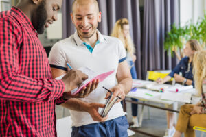 Two young men collaborating while taking notes in their notebooks