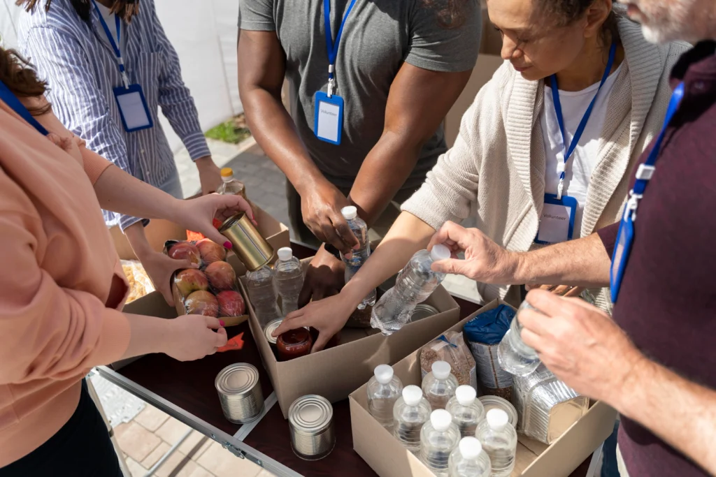 Diverse group of volunteers with badges collaboratively packaging food items together at outdoor community event