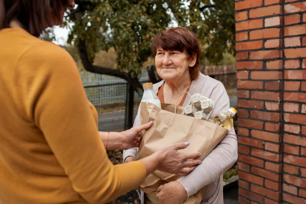 Elderly person receiving food donation in brown bag from a volunteer