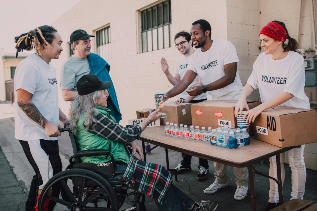 A group of volunteers assisting a person in a wheelchair with water and other donations.